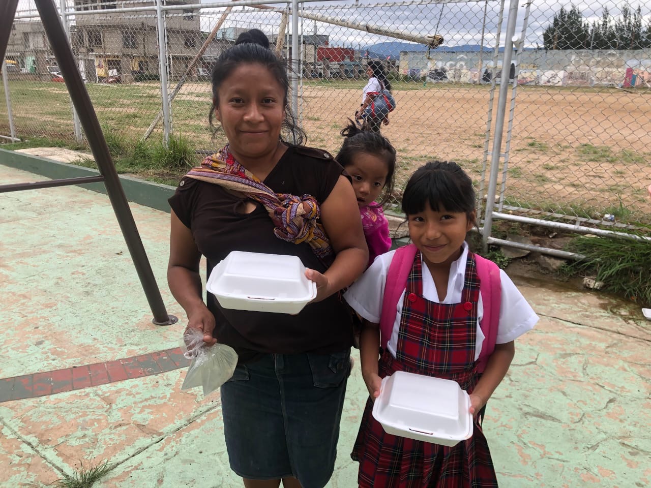 A mother and two girls holding meal containers outside